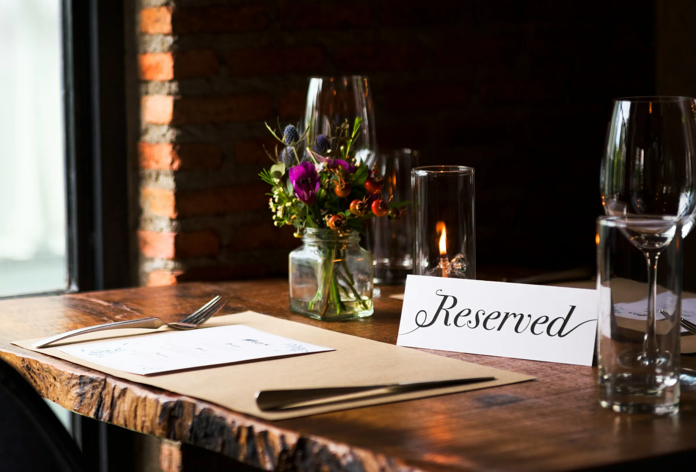 Une carte « Reserved » posée sur une table en bois dressée, avec un menu, une bougie et un petit bouquet de fleurs.